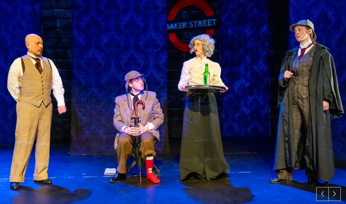 Four characters: from the left a bald man wearing a tie and a beige vest and pants, a man sitting won wearing one red sock, a woman carrying a tray with a green bottle on it, and a woman wearing deerstalker and a long dark coat. 