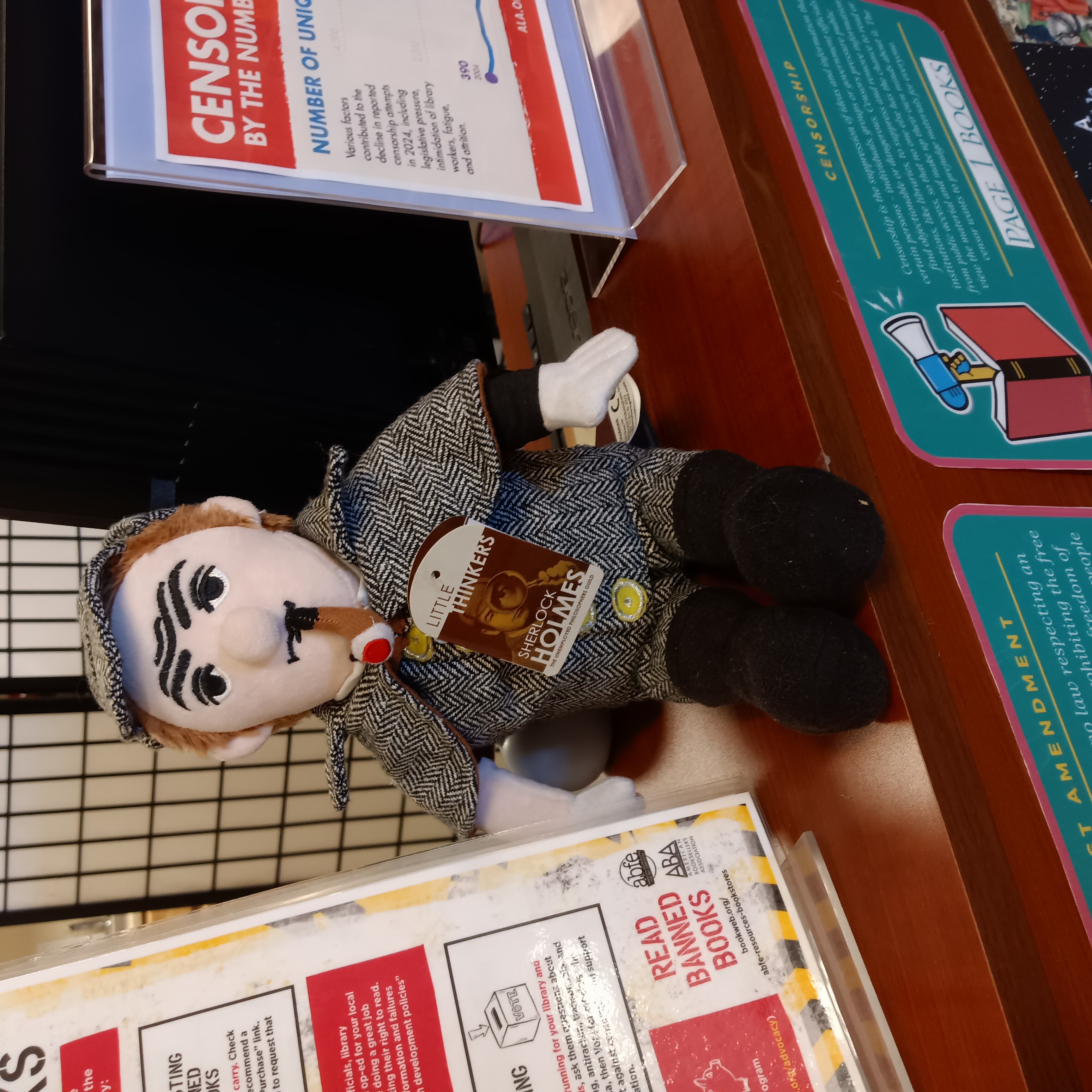 Sherlock Holmes doll with pipe, deerstalker and dark gray Inverness cape sitting on a shelf.