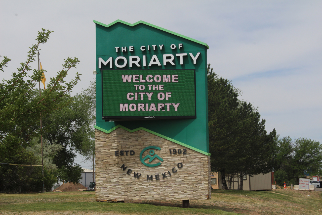 Large green sign that says in white block letters The City of Moriarty, and below that a video sign that says Welcome to the City of Moriarty, and below that block letters that say Established 1902 and New Mexico.
